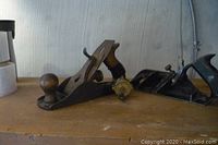 Two Stanley woodworking planes and a small fishing reel on a wooden shelf, showing overall condition and size.