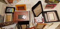 Top-down view of various assorted picture frames in multiple colors and sizes arranged on a white surface, showing diversity in materials and styles.