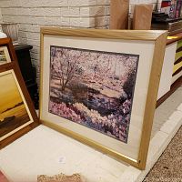 Framed landscape painting with pink, purple and green tones, depicting trees and a pond, set in a gold frame with cream matting.