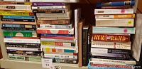 Photo of stacked classic books showing authors like Ayn Rand, George Orwell, John Steinbeck, and titles including 'The Moon' by Barry Gower, 'The Future of Folk Psychology', and others