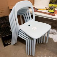 Six light blue plastic chairs stacked on each other in a storage area.