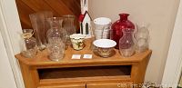 Photo of assorted glass and decorative vases and containers arranged on wooden cabinet.