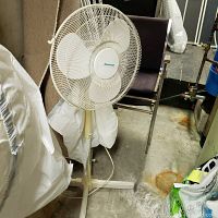 White Duracraft pedestal fan standing on the floor next to a chair and other household items.