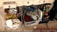 Plastic tubs and a black milk crate filled with assorted Christmas decorations, ribbons and gift wrapping materials under a white desk.