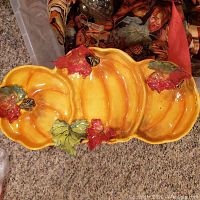 Orange ceramic pumpkin-shaped serving tray with leaf embellishments on carpeted floor.