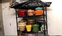 Overall view of three shelves filled with various gardening pots including ceramic, terracotta, plastic, and metal pots.