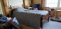 Twin wooden bed frame with headboard and footboard in a room setting covered with a patterned bedspread.