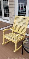 Single yellow wooden rocker chair with slatted seat and backrest, some paint wear visible.
