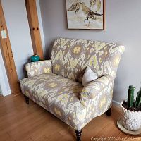 Front angle view of patterned loveseat with a wooden frame, placed against a wall with wooden floor beneath.