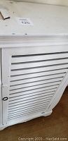 Close-up photo of the top and door details of the white antique pie cupboard showing wear and paint chipping.