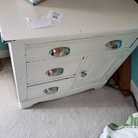 Front view of white wooden end table showing three drawers with silver cup handles and a cabinet door with a round knob.