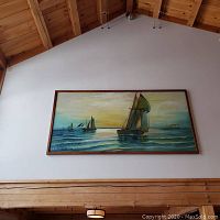 Framed wall mural of sailing ships hanging on a tall wall with wooden beams, showing full artwork and surrounding area for scale.