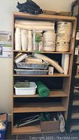 Full view of wooden shelving unit with all items including disposable plates, cups, trays, bubble wrap and garden supplies arranged on shelves.