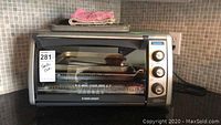 Black and Decker toaster oven placed on countertop with cloth on top and a key tag stating 'Toaster Oven'.