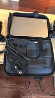 Open laptop case with HP laptop inside, power adapter cable visible