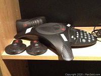 Polycom SoundStation 2 conference phone and components shown on wooden shelf.