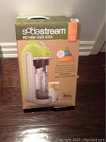 Front of the boxed SodaStream showing the green and white drinkmaker with carbonating bottle and product slogans.