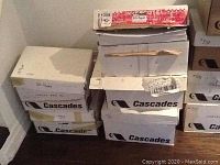 Five boxes of Cascades brand heavy laser paper stacked, one opened showing paper inside, stored on floor.