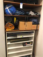 Closet shelf with rolled tents, mattress pads, cardboard boxes for camping gear