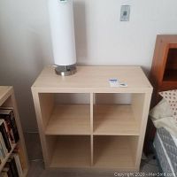 Light wood Ikea Expedit bookshelf with four open cubbies and a white lamp on top.