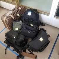 Photo showing various camera bags grouped together on floor with Samsonite luggage behind them