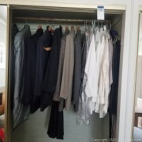 Closet with men's jackets, blazers, and shirts, some protected with plastic garment covers, several in neutral colors including black, navy, and gray