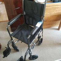 Front angle shot of the black manual wheelchair showing the metal frame, padded armrests, footrests, and seat fabric.
