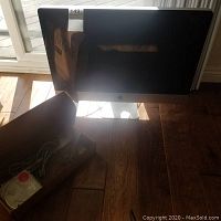 Front view of silver Apple iMac on wooden floor with box of accessories beside