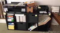 Wide shot of two printers, paper boxes, binders and rolled papers on shelf