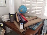 Photo showing the Cram's Imperial World Globe sitting on a table surrounded by several rolled paper and wall maps, along with a paper cutter and a wastebasket.