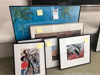 Photo showing all six framed wall art pieces arranged side by side, visible through a glass window reflecting the surroundings