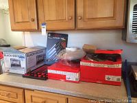 Photo of multiple boxed kitchen items including Black+Decker toaster oven box, Rogers cutlery set box, and two red and white boxes for Fissler cookware items on a countertop.