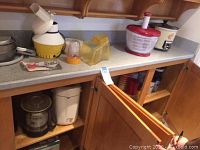 Countertop with assorted kitchen appliances including citrus juicer, salad spinner, blender parts, and stand mixer base.