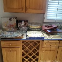 Wide view of assortment of serving platters and bowls on kitchen counter showing stacked trays, clear and decorative bowls