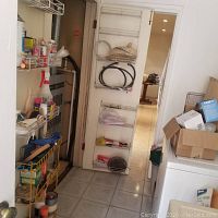 View of a narrow room with multiple wall-mounted racks holding assorted cleaning supplies and light bulbs, a washer or dryer partially visible on the right.