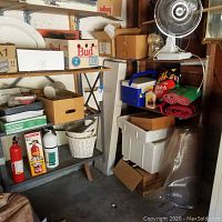 Shelves with assorted garage accessories including fire extinguishers, boxes, cooler, blankets, fan, painting supplies and storage baskets.