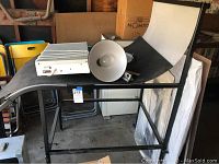 Photo of black curved photo table with light box and reflector lamp on top, showing overall setup