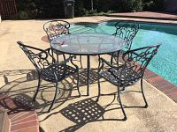 Full view of round glass top patio table with four metal chairs placed on poolside patio.