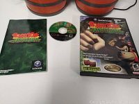 Top-down view of instruction booklet, game disc, original game case showing Donkey Kong Jungle Beat cover art, and DK Bongos drums controller.