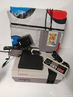 Nintendo NES console, controller, power adapter, black accessory, Track and Field game cartridge and exercise mat (pad) displayed together.