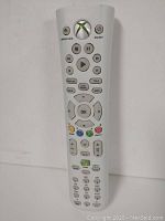 Front view of the wireless Xbox 360 DVD remote showing all buttons clearly including power, Xbox logo, media controls, gaming colored buttons, and numeric keypad.