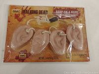 Full packaged view of The Walking Dead soap-on-a-rope, showing four ear-shaped soaps attached to a rope, sealed in original packaging with branded background.