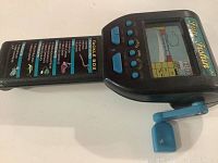 Side angle showing screen, buttons, blue crank, and tackle box cover with lure illustrations.
