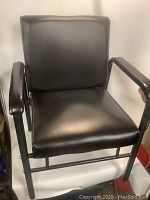 Front view of black leather salon chair with metal frame and armrests