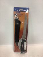 Front view of Shimano fillet knife in original packaging showing blade, handle and sheath along with brand and product details.
