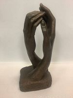 Front angle of bronze sculpture showing two joined hands with fingers intertwined, mounted on rectangular base.
