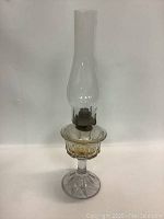 Full view of the glass oil lamp showing the clear glass chimney and textured amber-tinted base with metal burner.