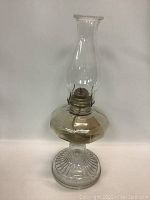 Full view of oil lamp showing glass chimney, metal burner, and glass reservoir on ribbed base.