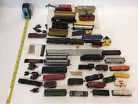 Overview of most items laid out, including engines, tank cars, freight cars, and cabooses in varied colors and conditions with tape measure for scale.