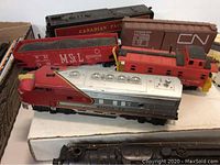 Model trains laid out on a white surface showing Santa Fe locomotive, Canadian Pacific and Canadian National cars, red caboose and MSL gondola car.